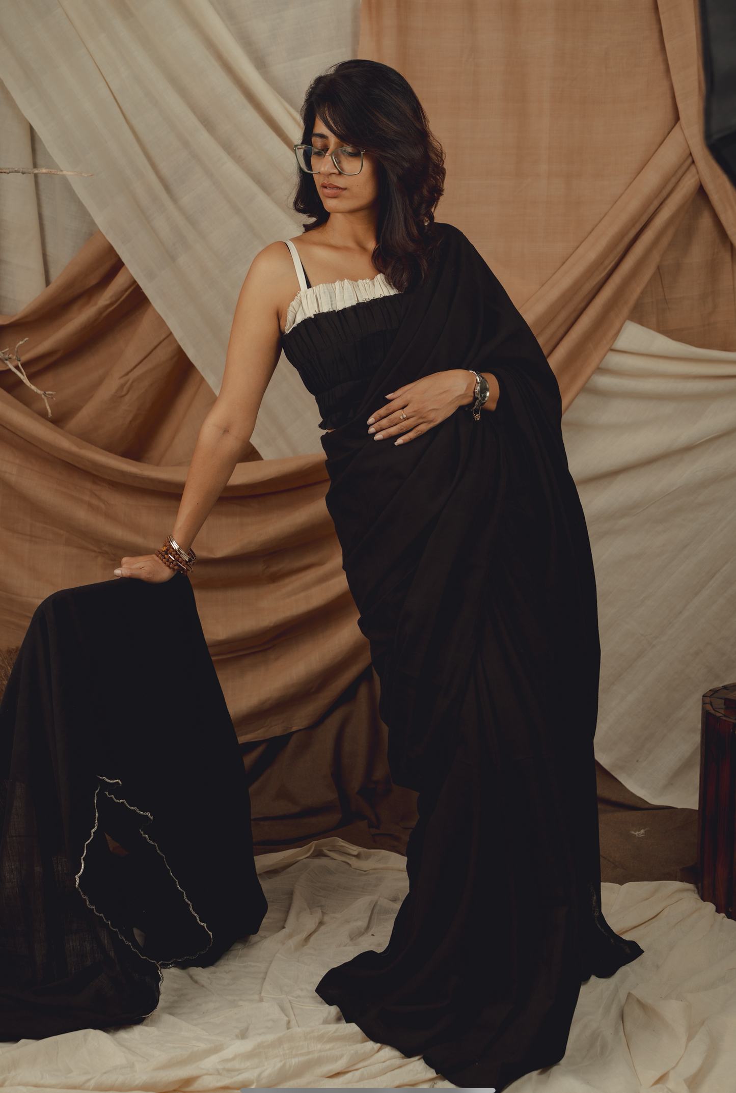 Woman in a black saree with a white blouse against draped fabric background